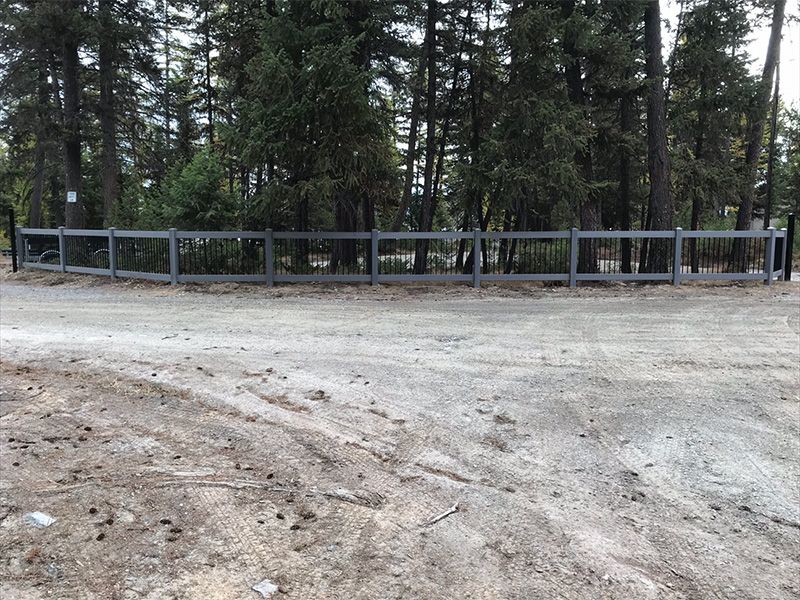 A wooden fence surrounds a dirt road in the middle of a forest.