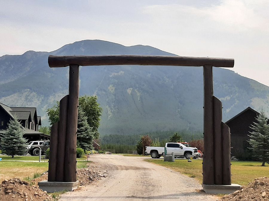 A wooden archway leading to a dirt road with mountains in the background