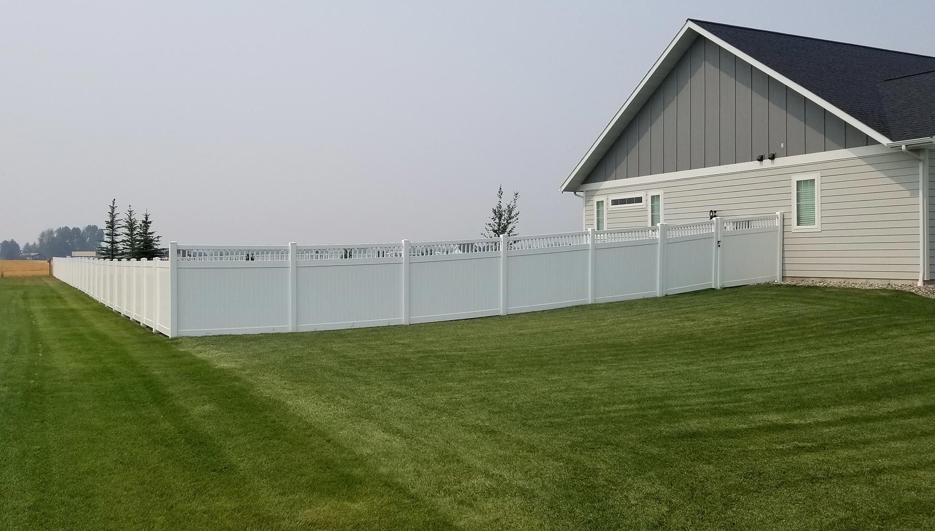 A white fence surrounds a lush green lawn in front of a house.