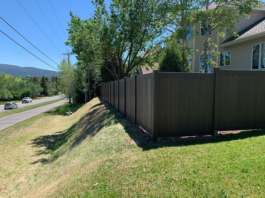 A wooden fence surrounds a grassy hill next to a house.