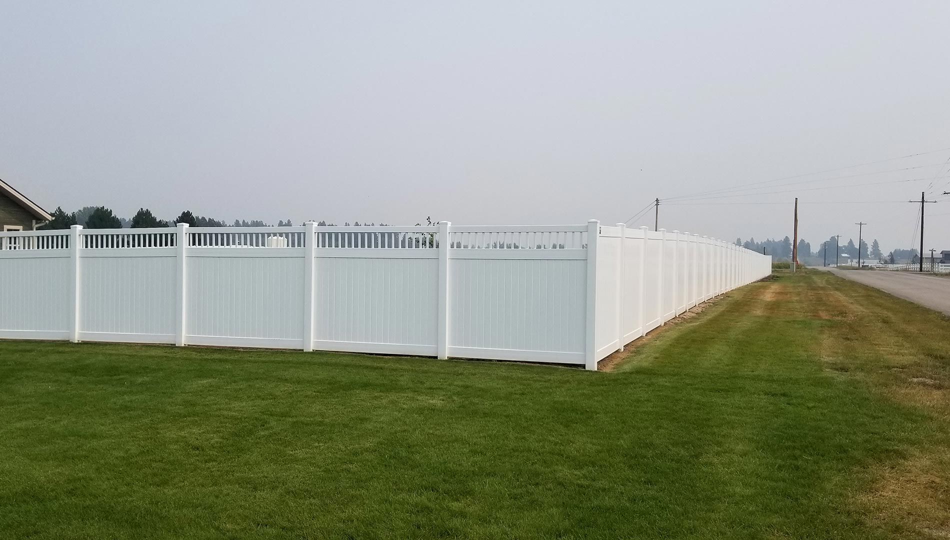 A long white fence surrounds a lush green field.