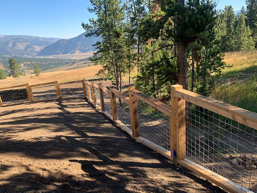 A wooden fence surrounds a dirt road with mountains in the background.