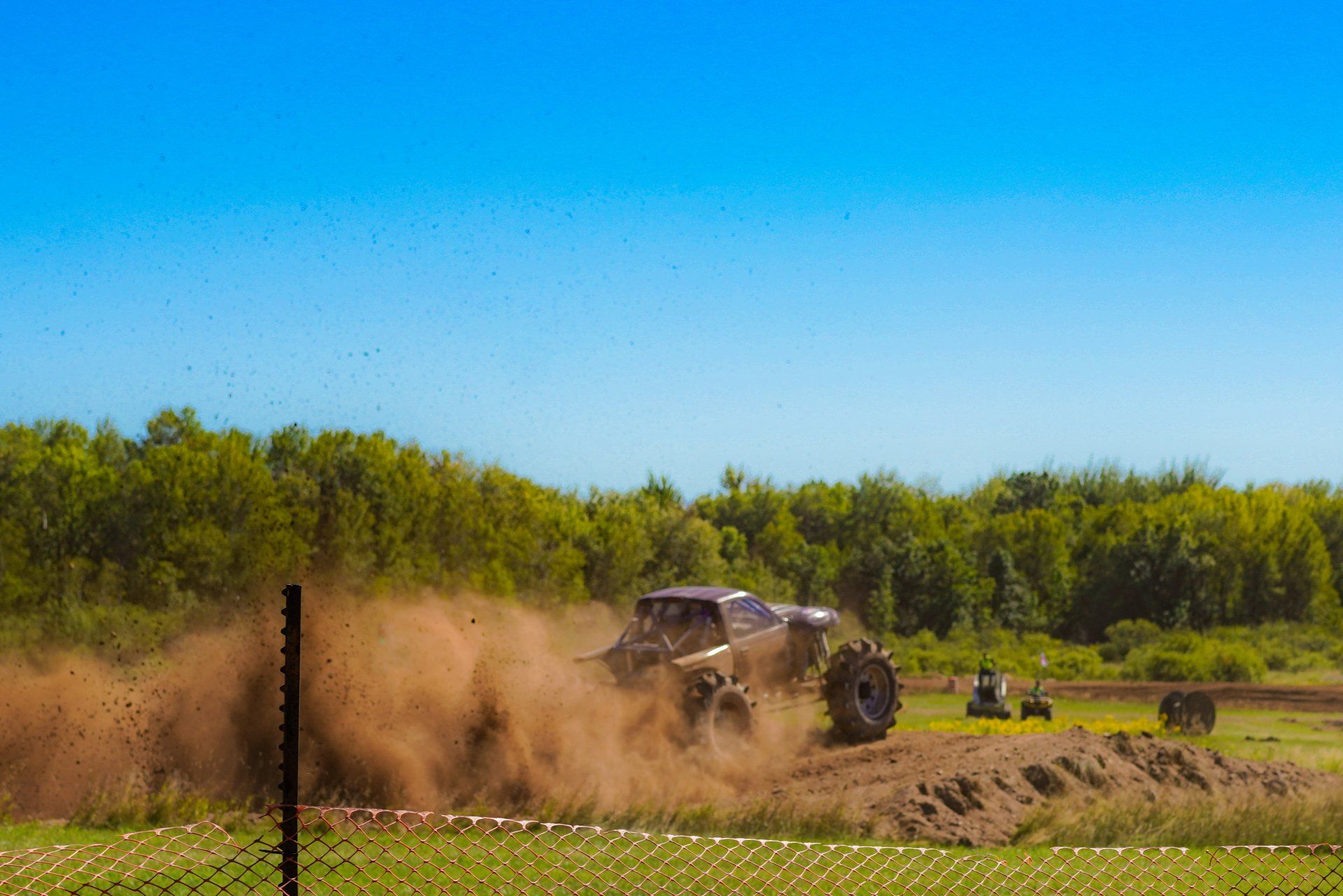 Off-road truck kicking up dust on a dirt track with green trees and blue sky behind it