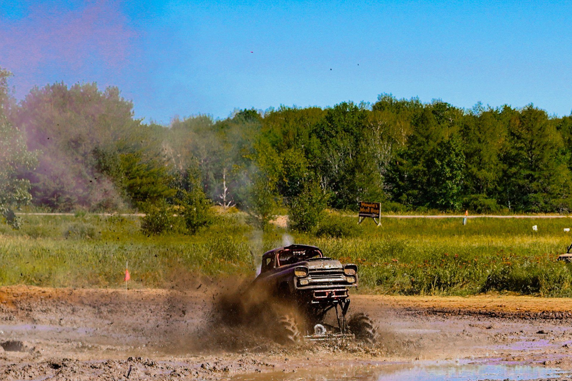 ATV splashing through muddy water in a rural field with trees in the background