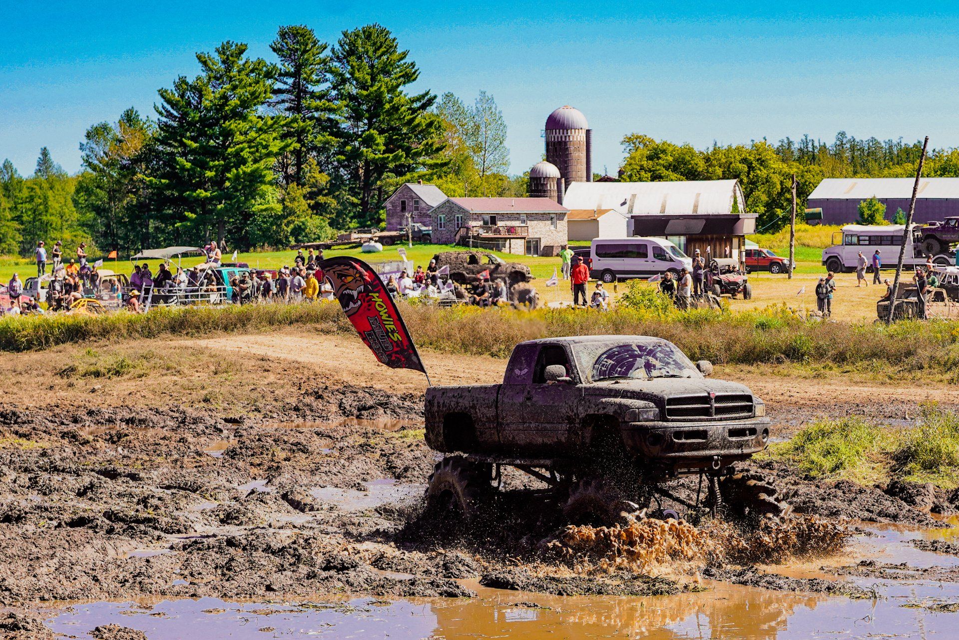 Mud-covered pickup truck splashing through a muddy pit at an outdoor truck event