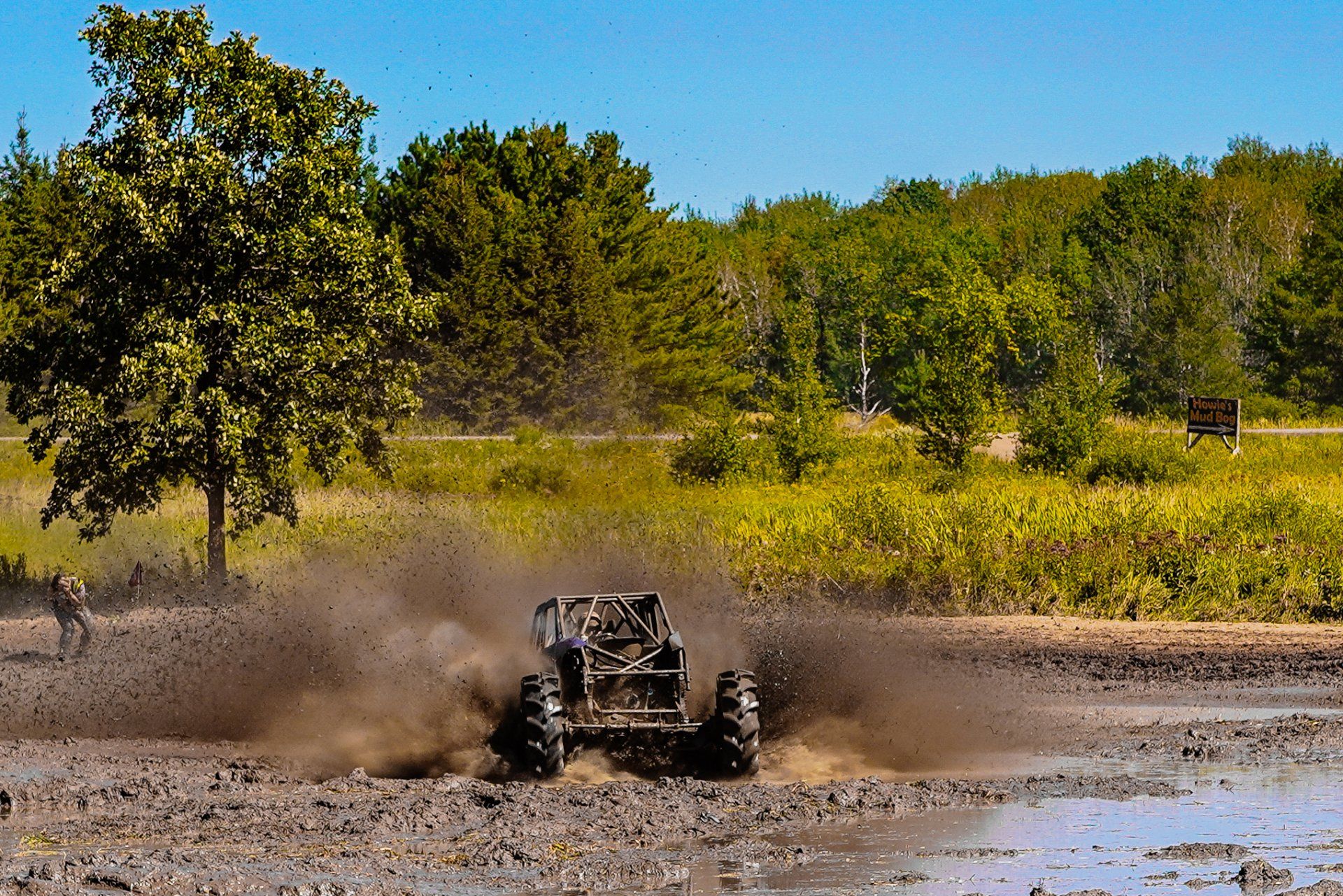 Off-road buggy splashing through muddy water on a dirt track, with dust and trees in the background