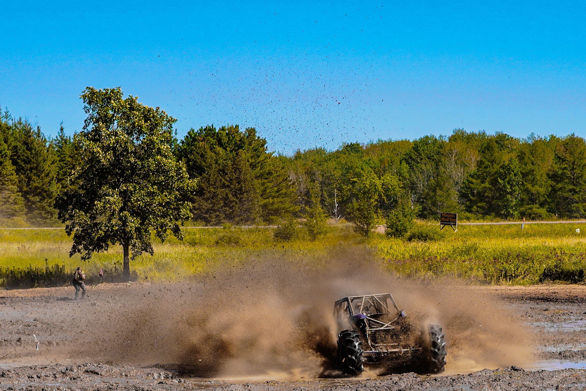 Off-road buggy racing across gravel, kicking up a dust cloud under a blue sky.