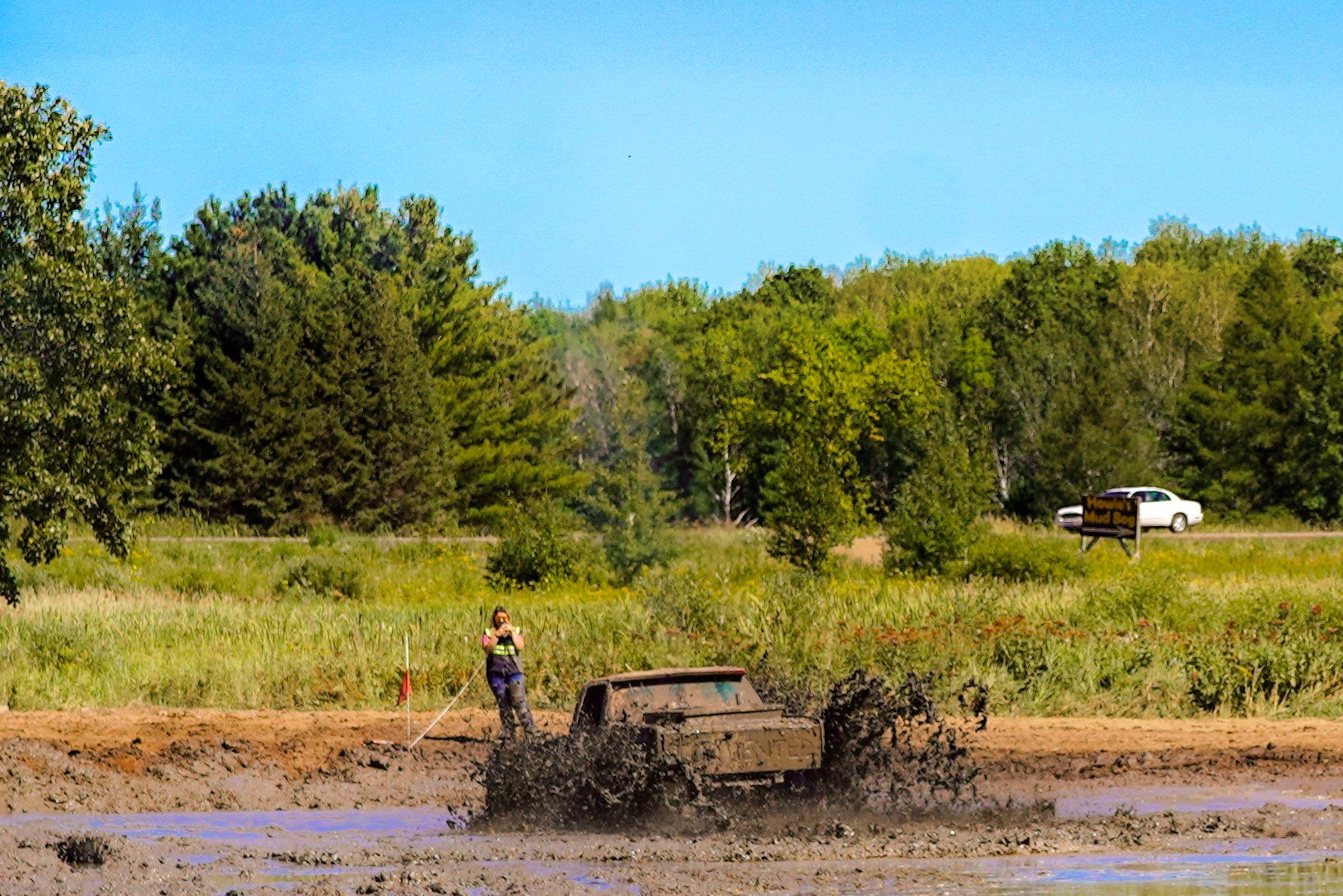 Off-road vehicle splashing through muddy water near a grassy field and trees