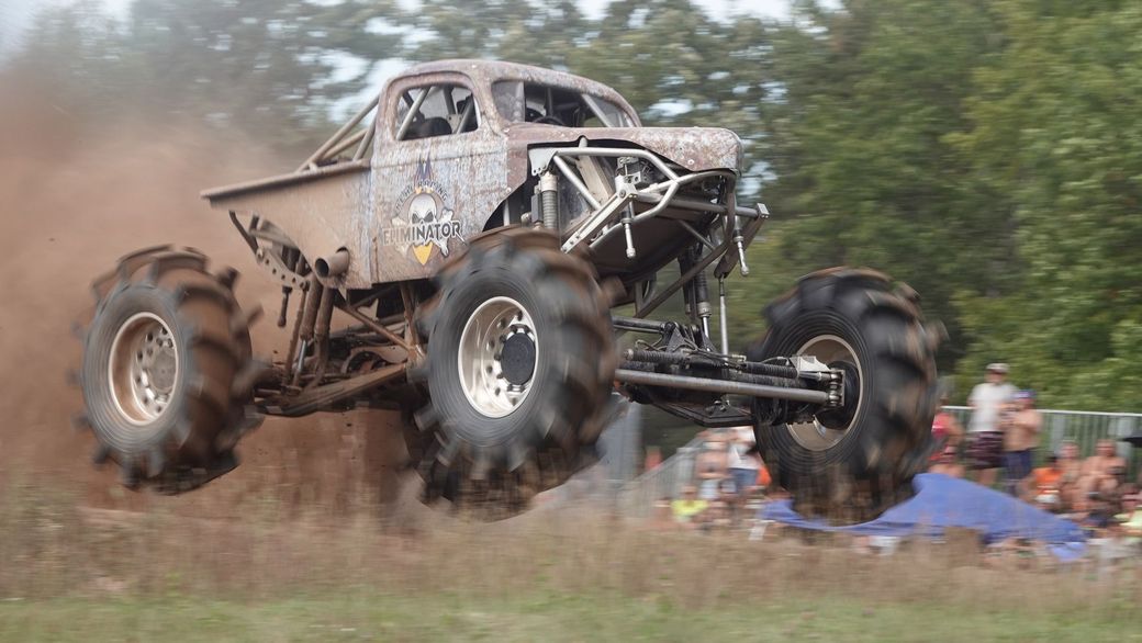 Monster truck airborne over muddy track, kicking up dirt at a motorsport event
