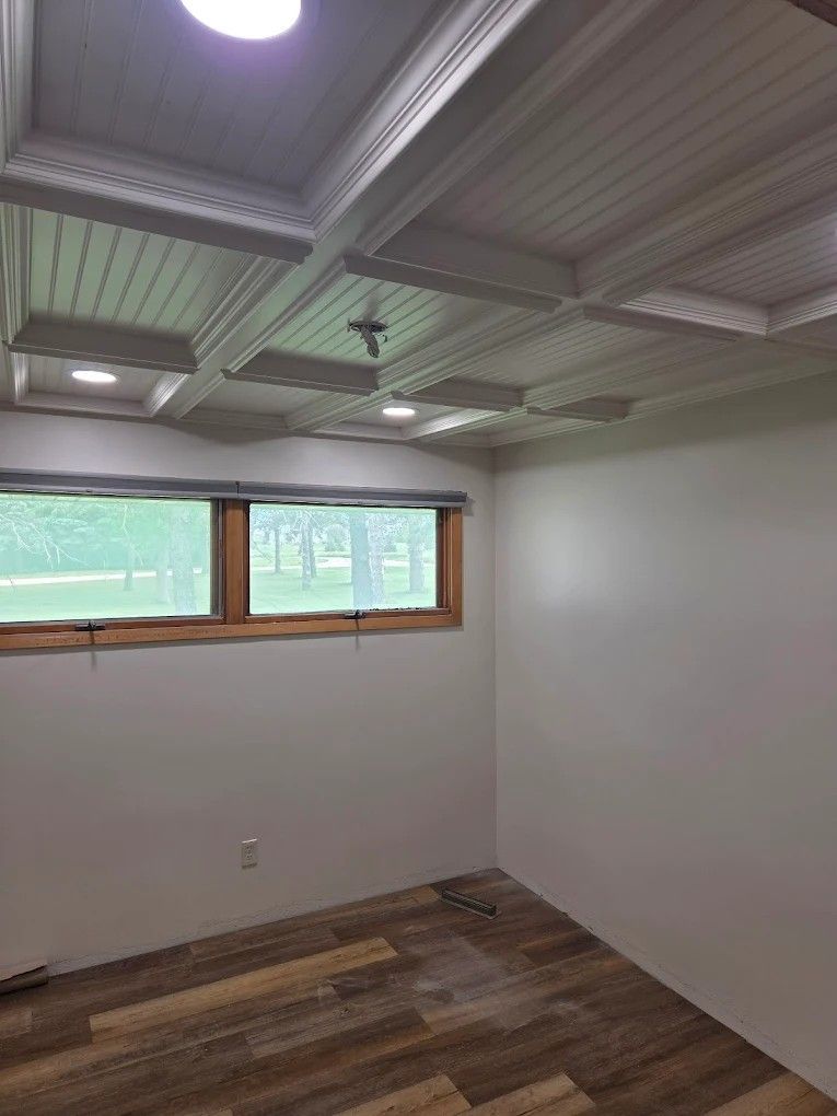 Empty room with white walls, wood-look floor, and a small window under a bright ceiling light.