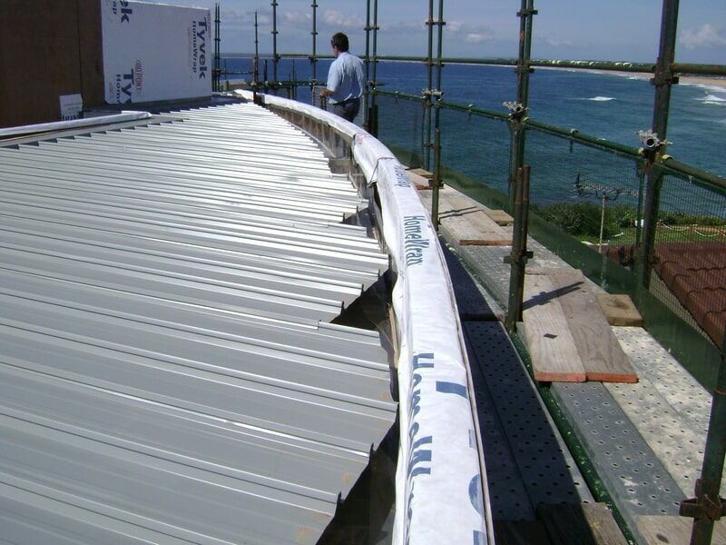 A Man Standing on Top of A Metal Roof with A Scaffolding Around It — R&M Sheetmetal Nowra Metal Roofing in South Nowra, NSW
