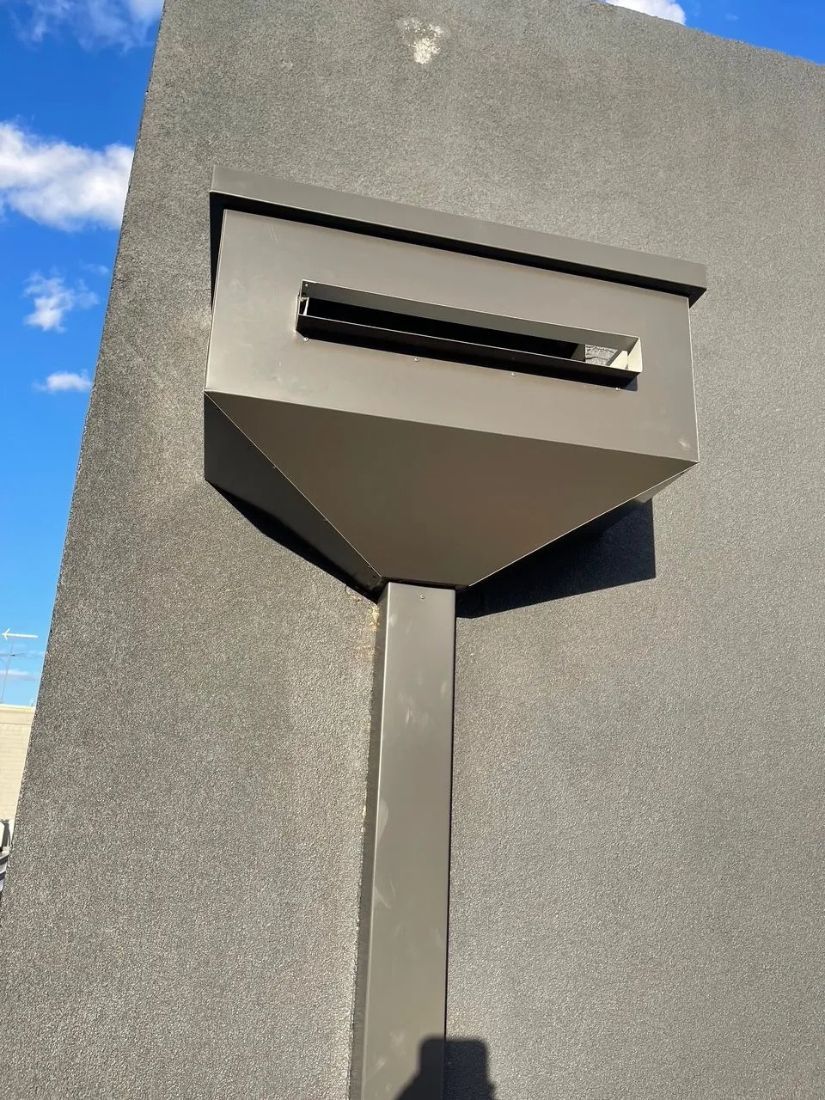 Gray metal mailbox mounted on a textured, gray wall with a blue sky background. — R&M Sheetmetal Nowra Metal Roofing in South Nowra, NSW