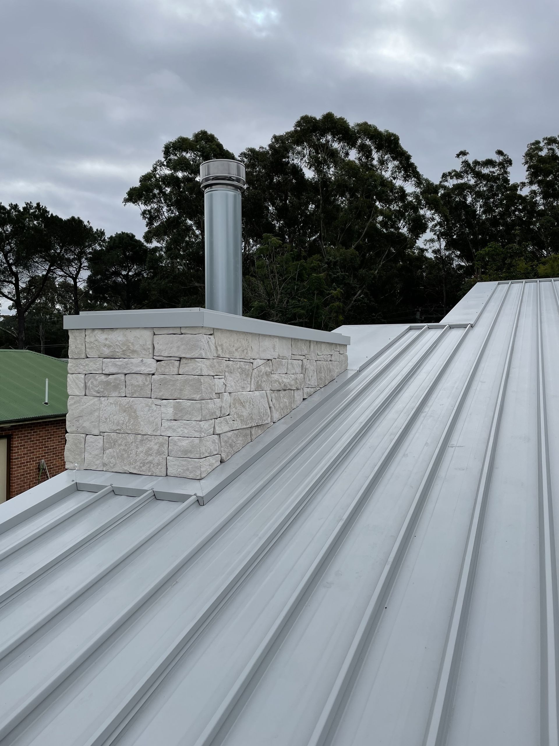 Chimney on a metal roof. A stone base supports a silver chimney pipe. Overcast day. — R&M Sheetmetal Nowra Metal Roofing in South Nowra, NSW