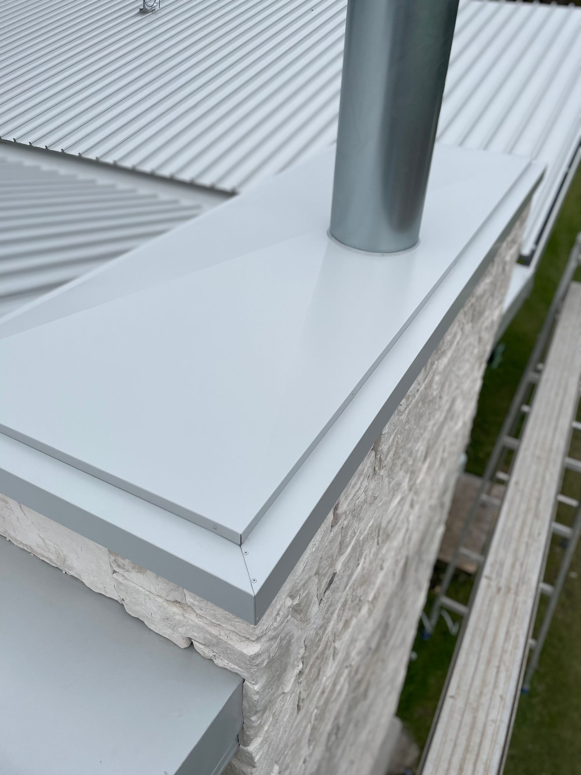 Close-up of a chimney with light grey metal flashing and a metal flue on a corrugated metal roof. — R&M Sheetmetal Nowra Metal Roofing in South Nowra, NSW