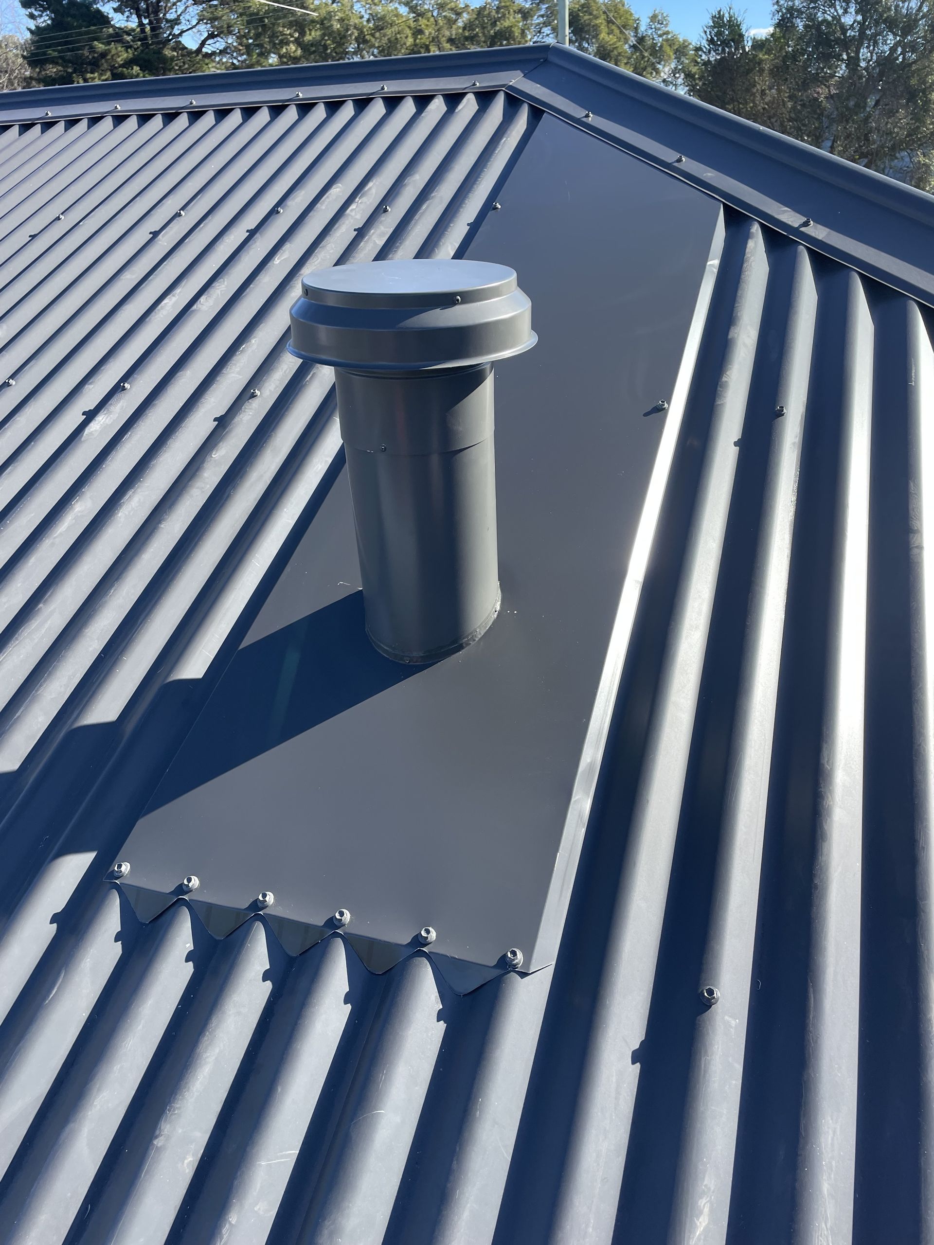 A gray vent pipe on a matching corrugated metal roof with surrounding flashing. — R&M Sheetmetal Nowra Metal Roofing in South Nowra, NSW
