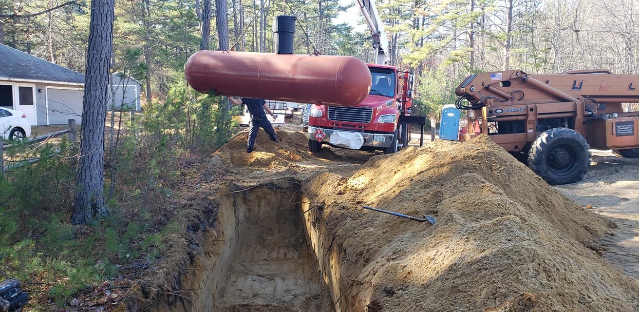 A red fuel tank is being lowered into a deep trench by a crane. A truck and a construction site are also in view.