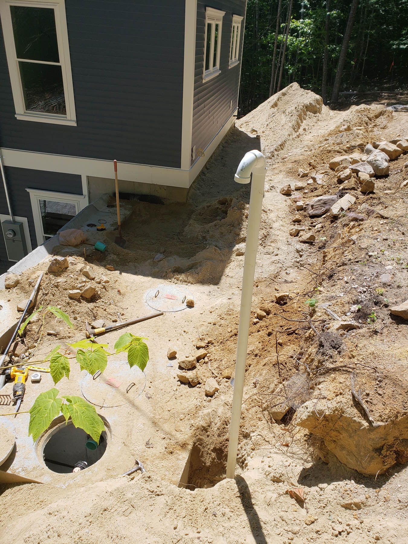 Construction site next to a blue house. A white pipe is in the foreground.