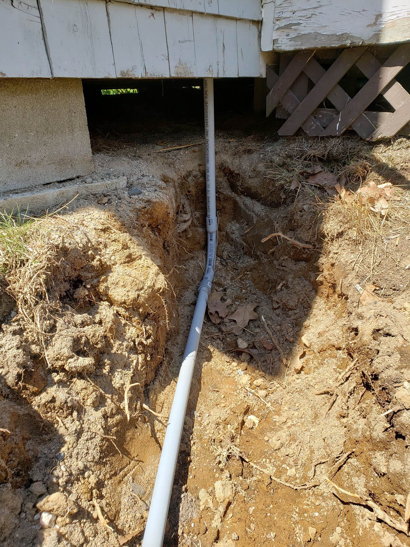 Gray conduit in a trench, running from under a house into the dirt.