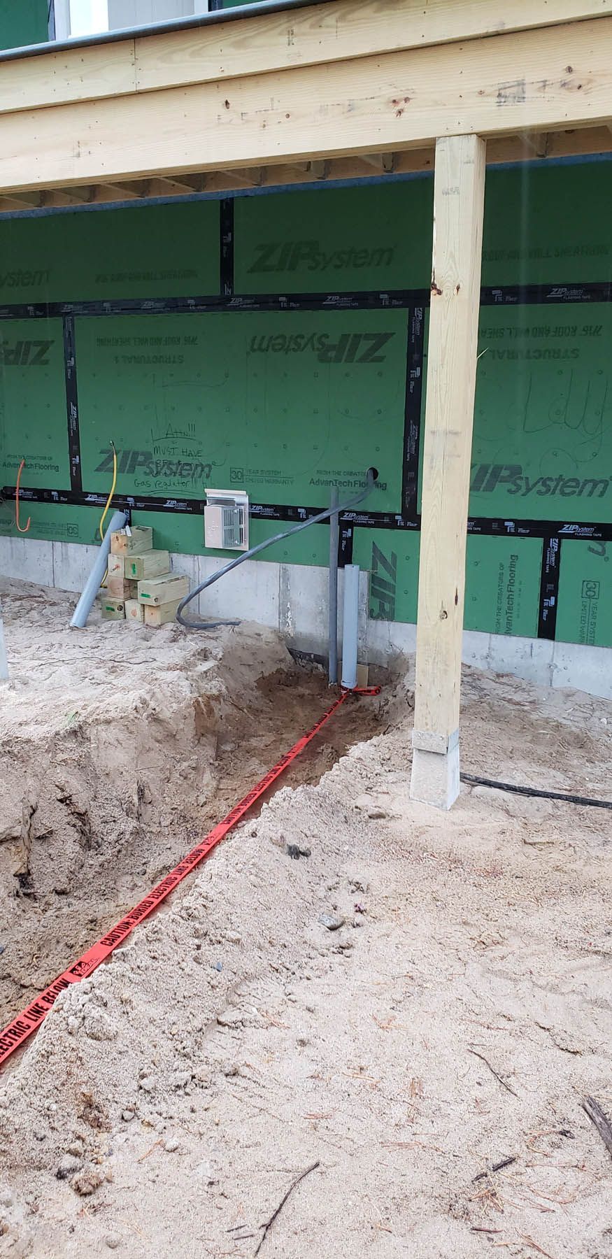 Construction site: red electrical conduit in a trench, wooden posts, green sheathing, sand.
