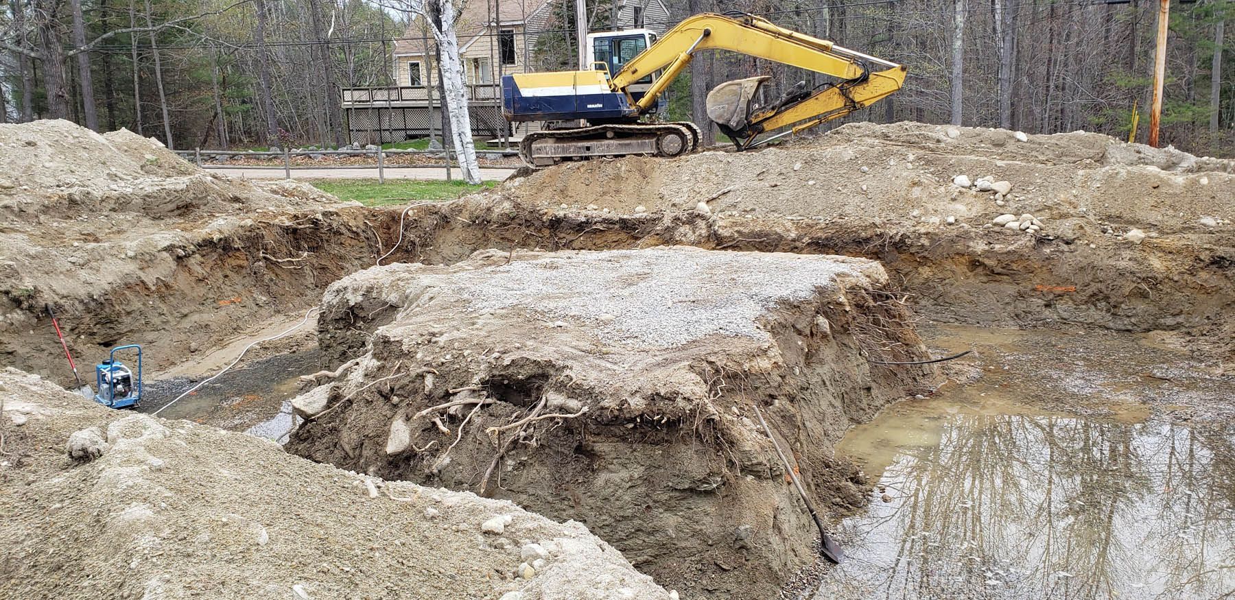 An excavator is digging a construction site foundation, surrounded by dirt and mud.