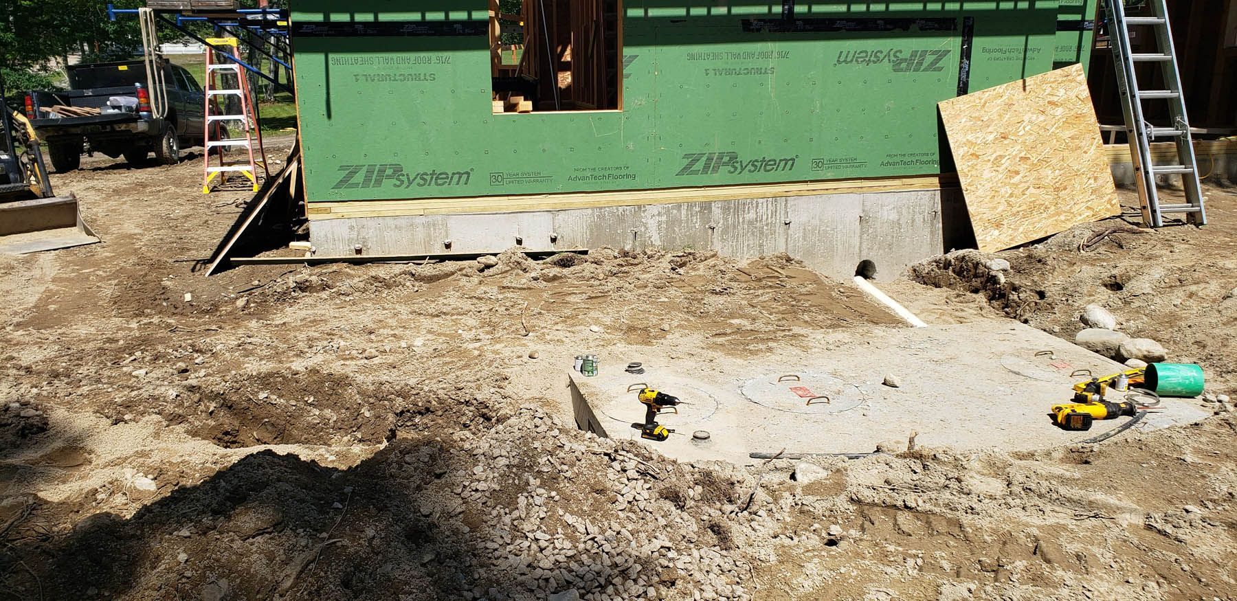 Construction site, unfinished building with green siding, dirt and tools.
