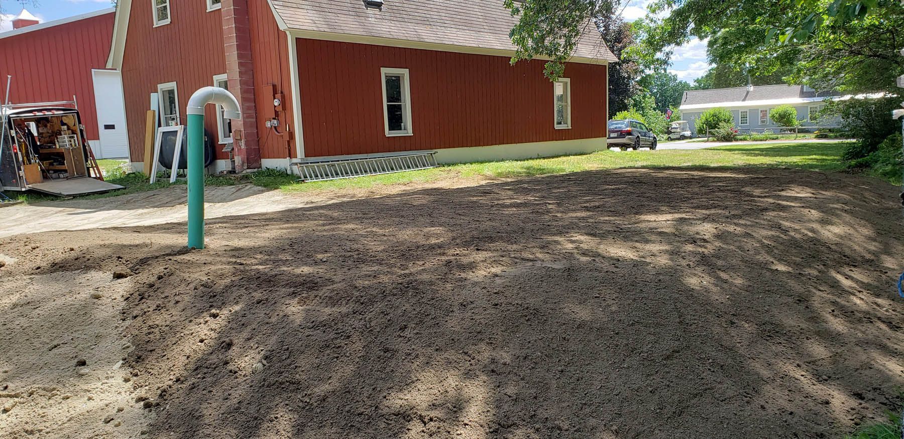 A red barn with a large dirt area in front. Green pipe in the foreground.