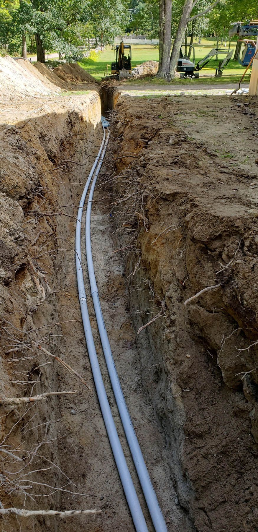 A trench with two grey pipes, likely for utilities, running through it outdoors.