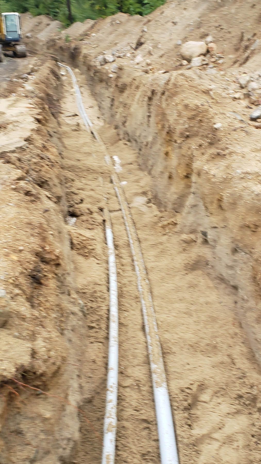 Trench dug in earth with white pipes running through it, likely for utilities, in a construction site.
