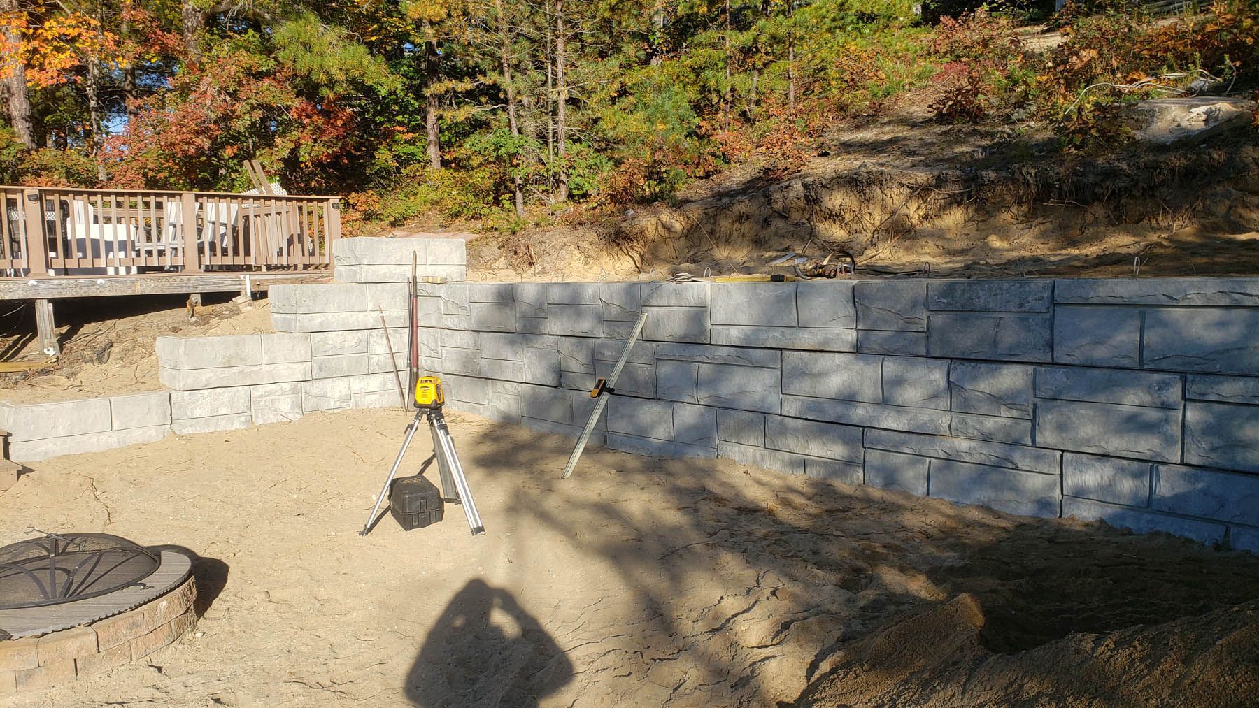 Retaining wall construction, with a laser level on a tripod in front.