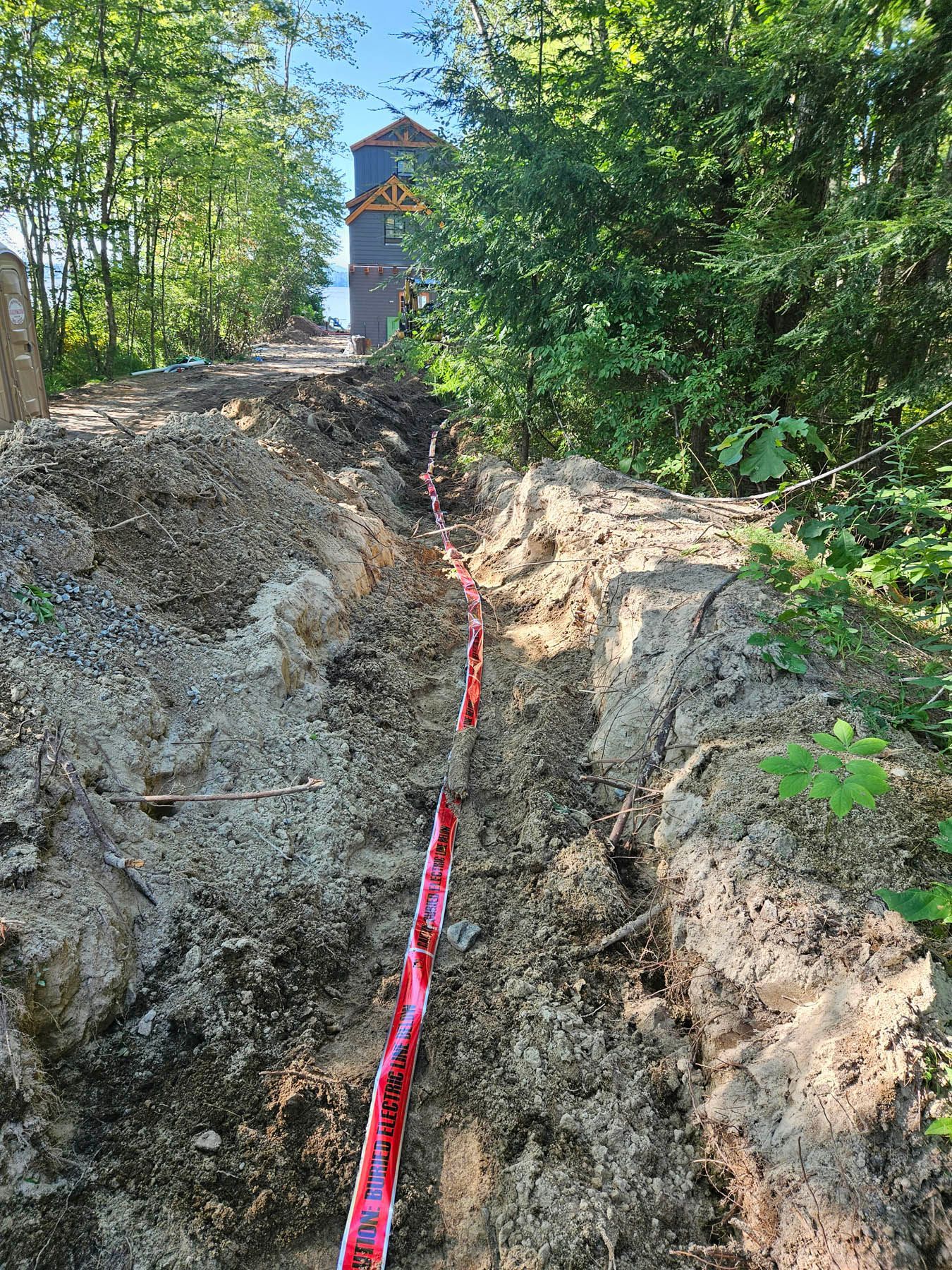 A steep, dirt path with red caution tape leads up to a tower in a wooded area.