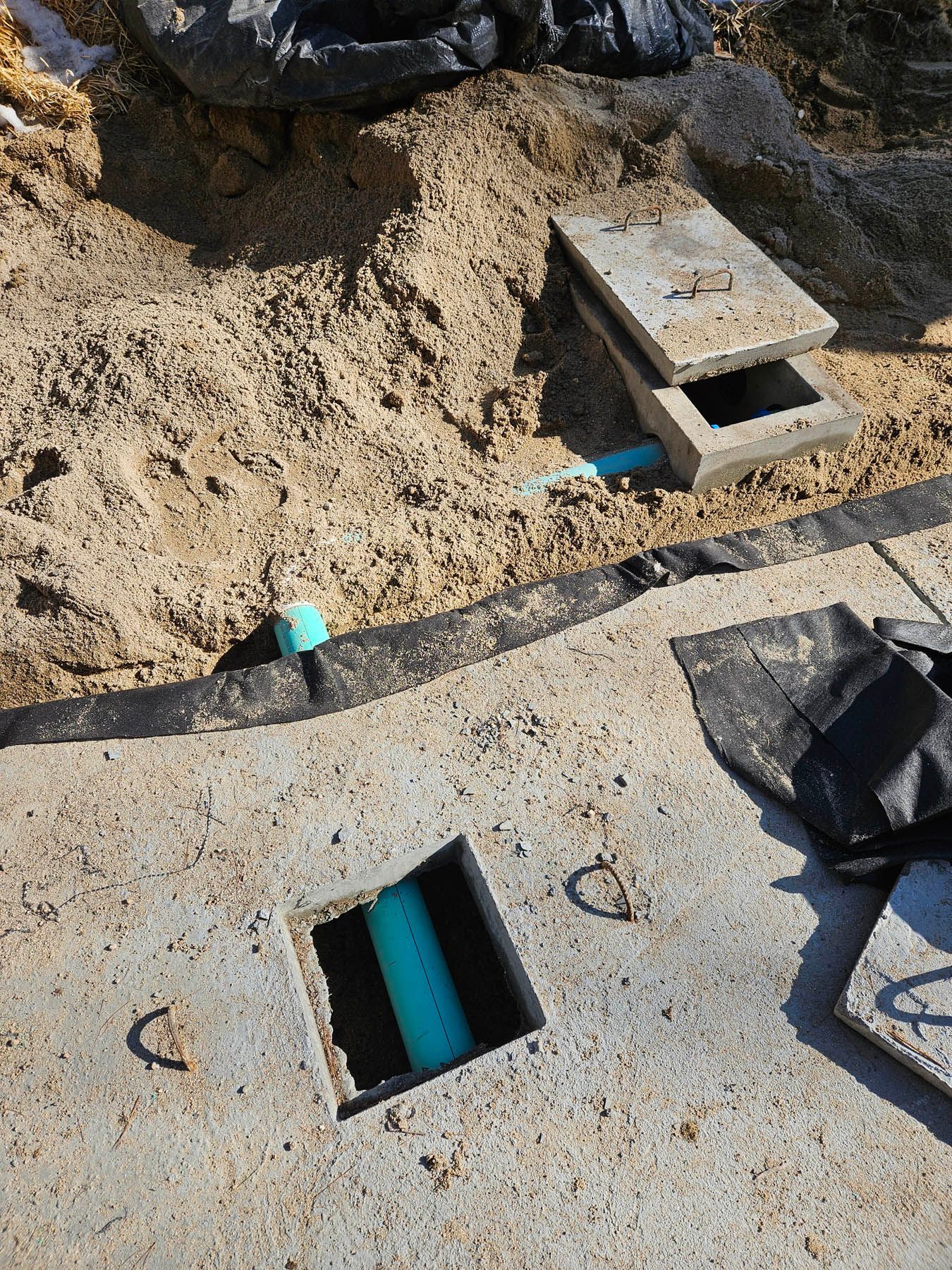 Concrete drainage work in progress: open box, pipe, sand, partially uncovered concrete.