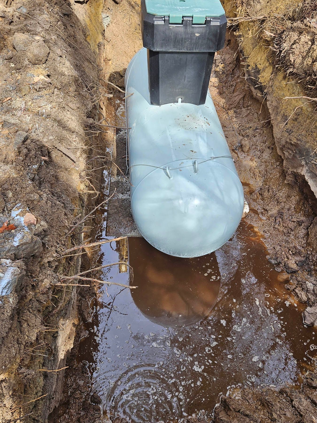 Underground propane tank with a cracked plastic covering in a water-filled trench.