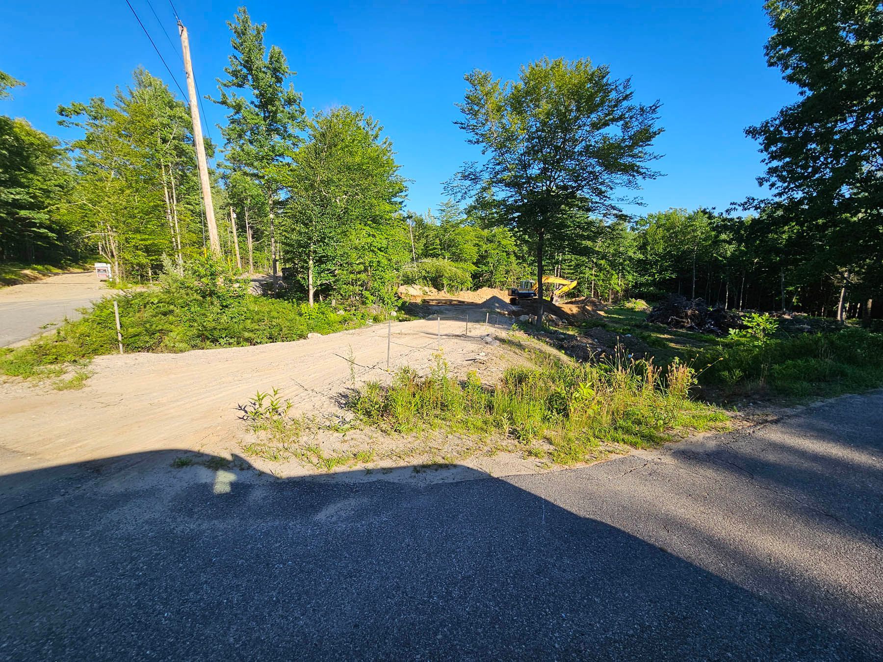 Gravel road intersection with a cleared area, trees, and blue sky.