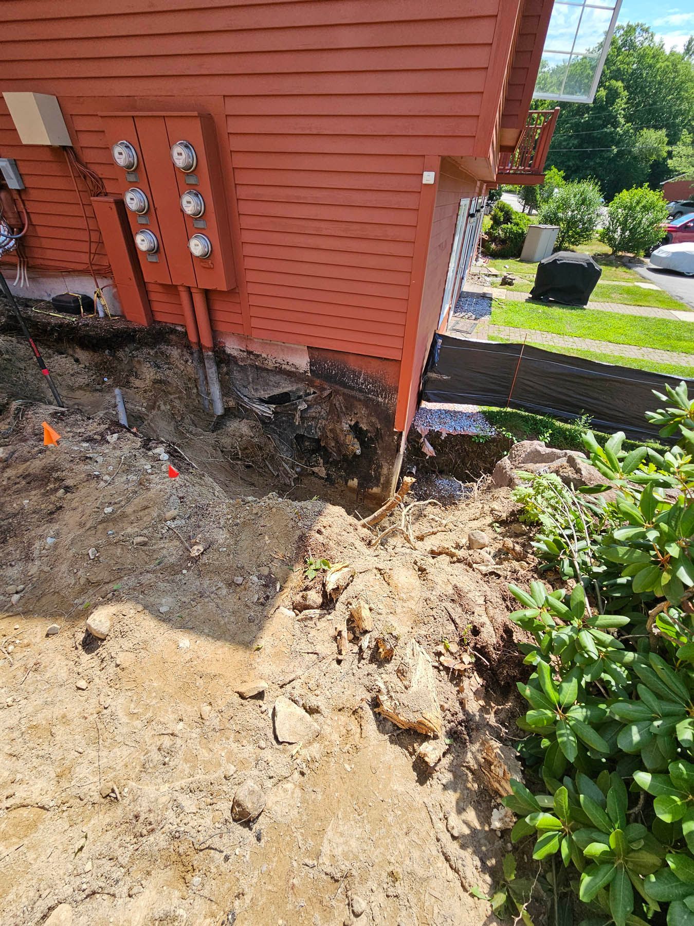Excavation next to a red building with electrical boxes; dirt, foundation visible.