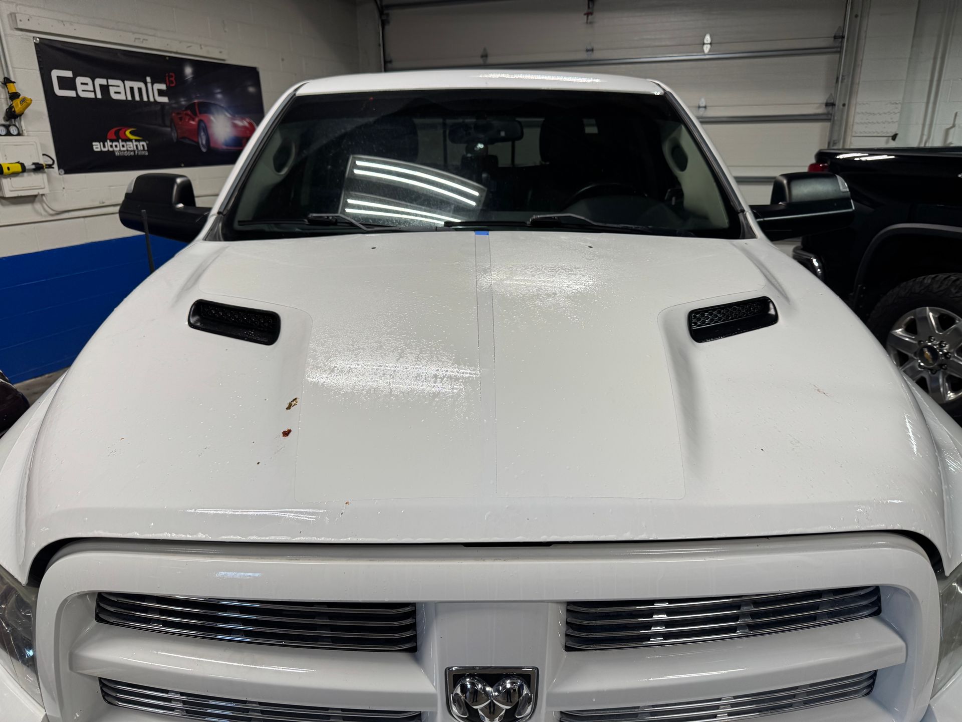 White pickup truck hood with hood scoops. Ceramic coating logo visible in background.