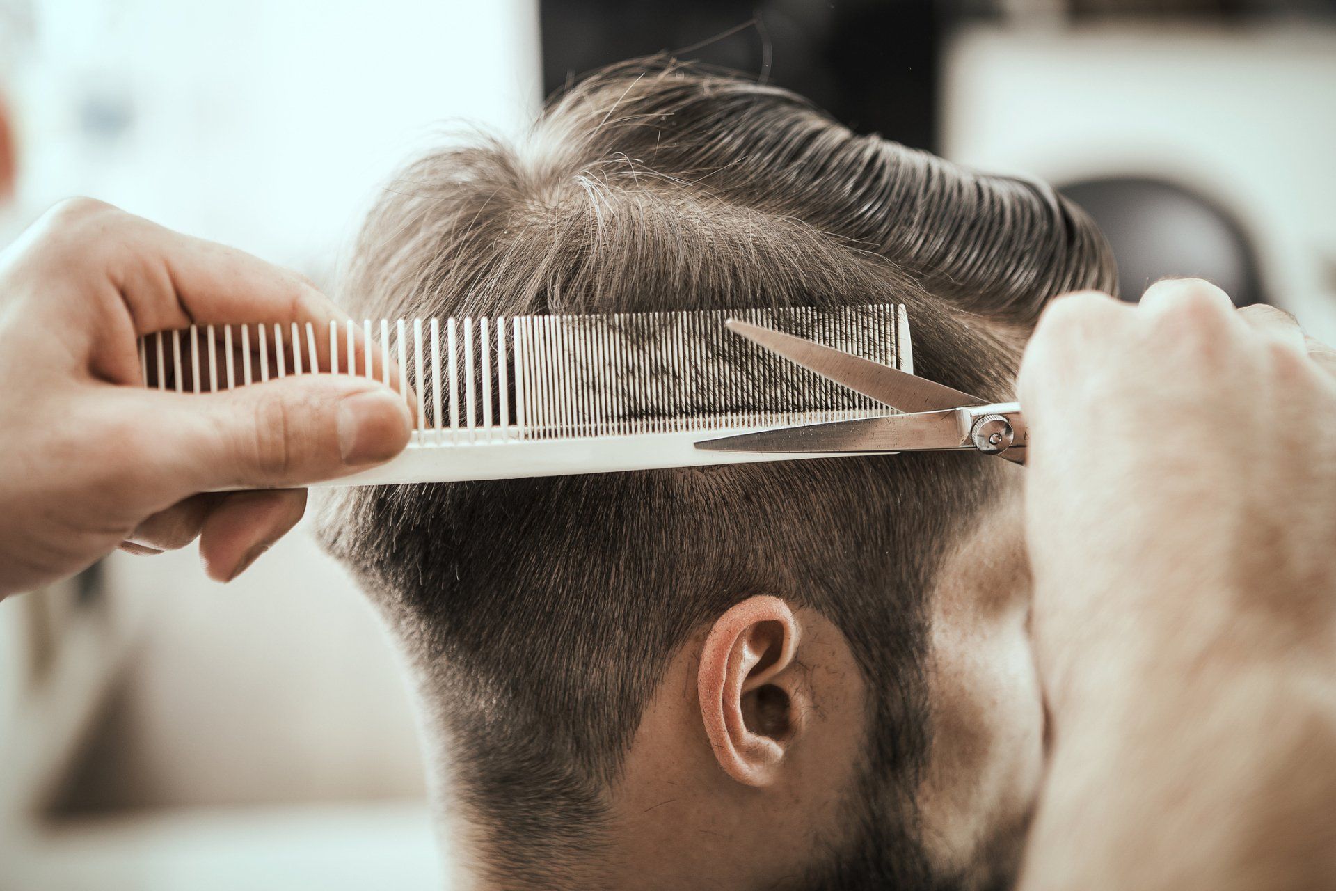 Primo piano di un barbiere che usa forbici e pettine per tagliare i capelli di un uomo.