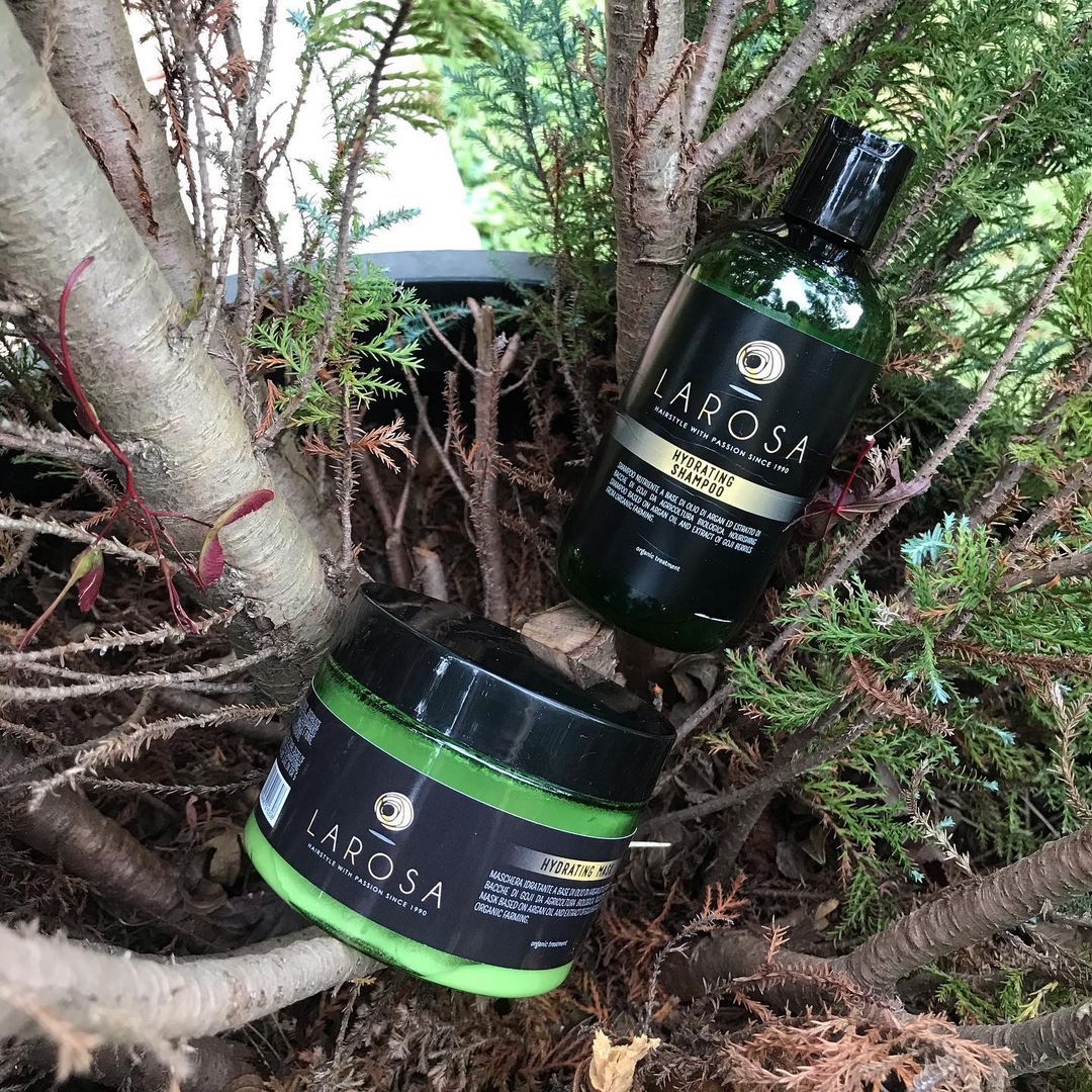 Due prodotti per la cura dei capelli Larosa sono appoggiati su un ramo d'albero, con etichette verdi e nere.