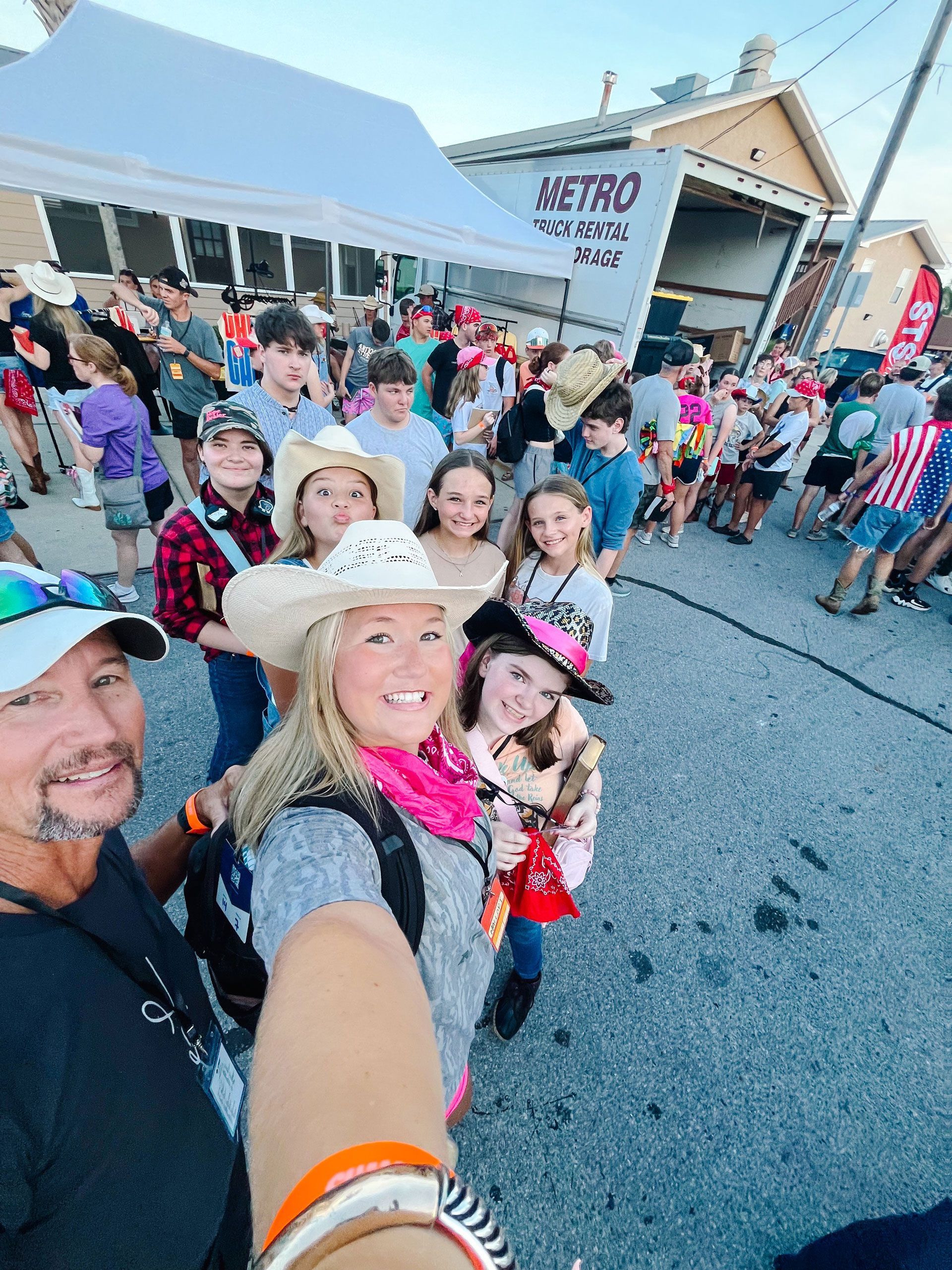 Crowd gathered outside a building, with smiling people posing for a selfie in the foreground.