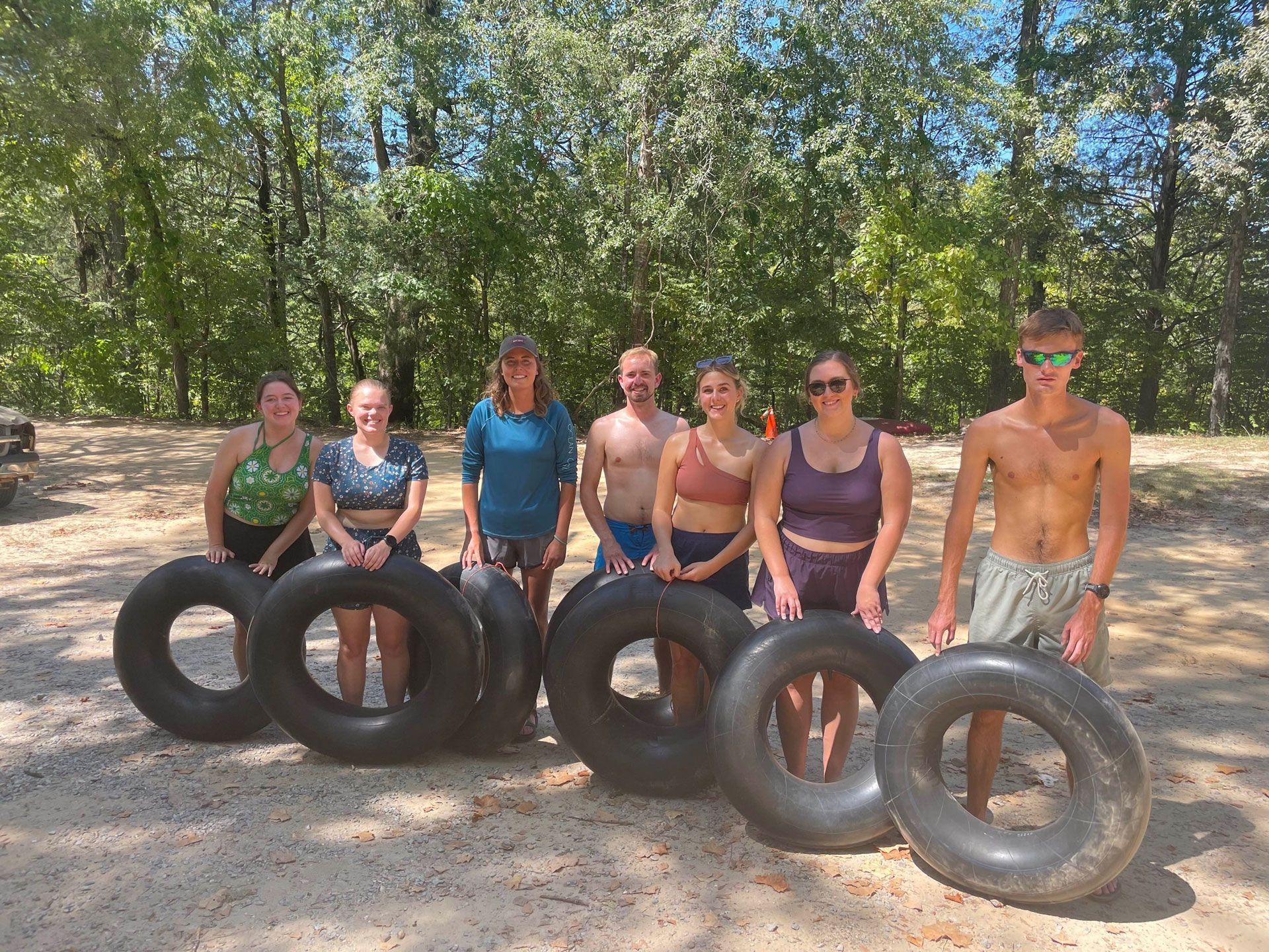 Group sitting behind stacked tires in a sunny wooded outdoor setting