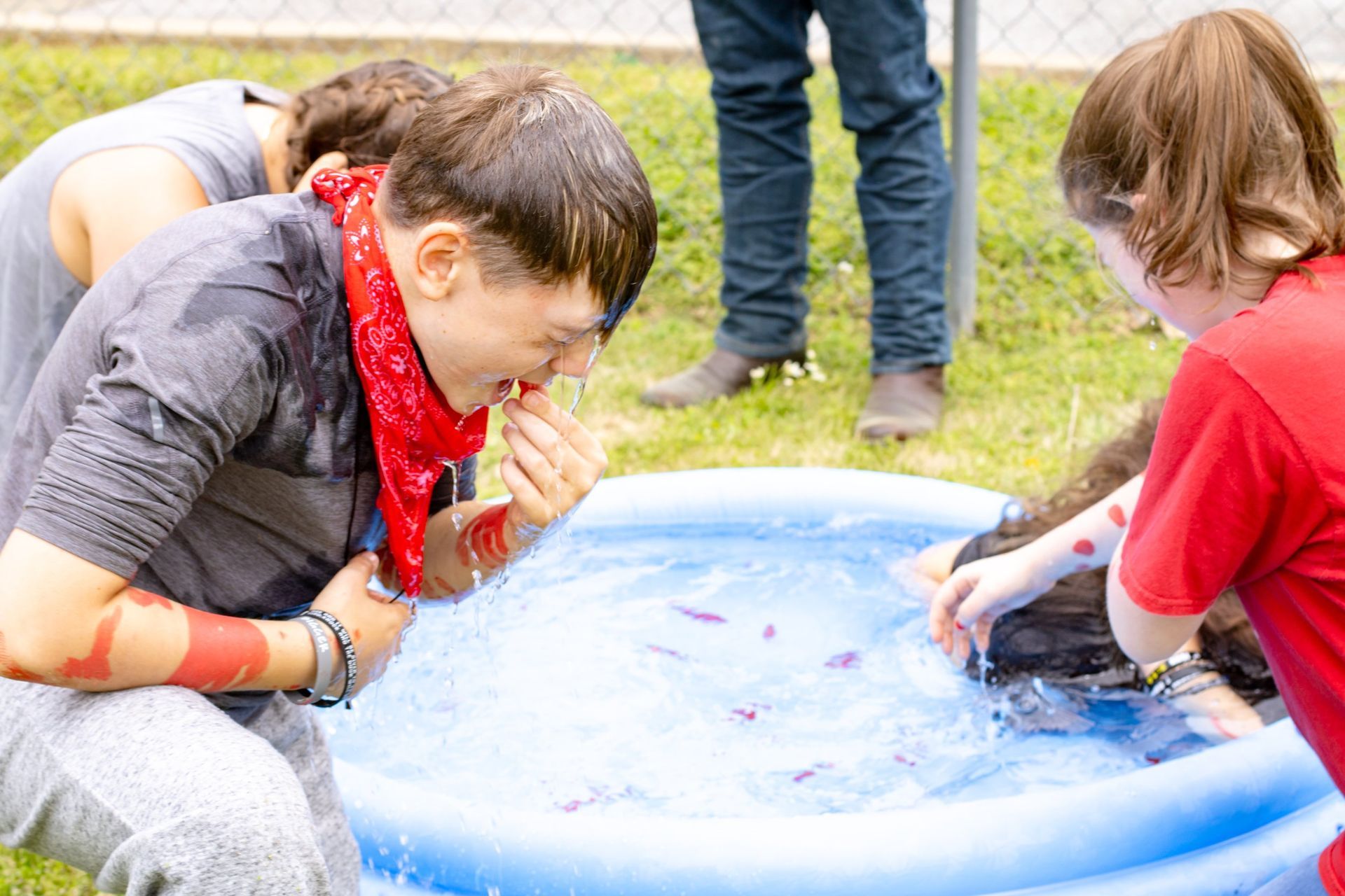 Children leaning over a blue inflatable pool, playing with water and ice outdoors