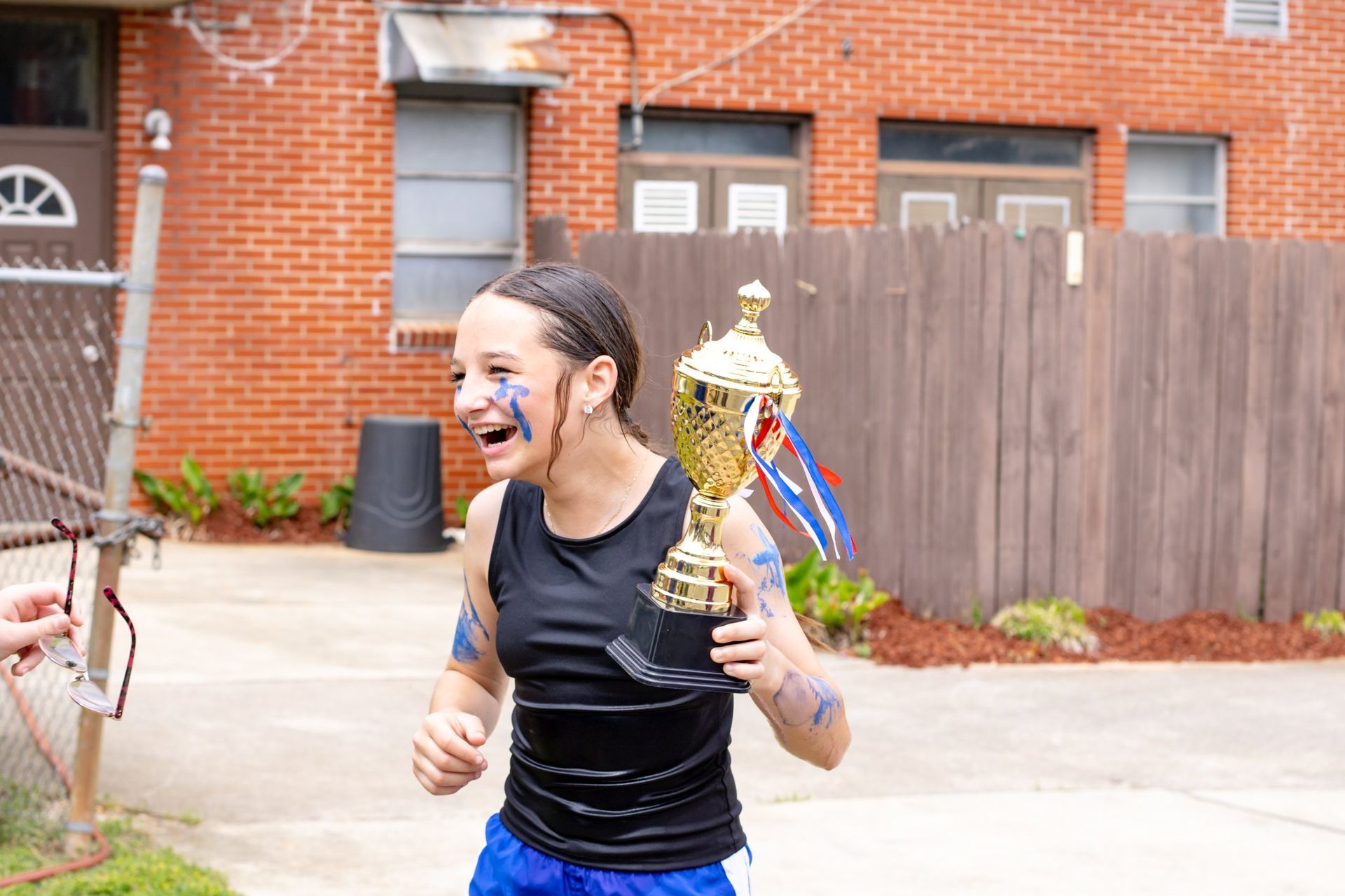 Runner holding a trophy and smiling, with face paint, in a driveway outside a brick house