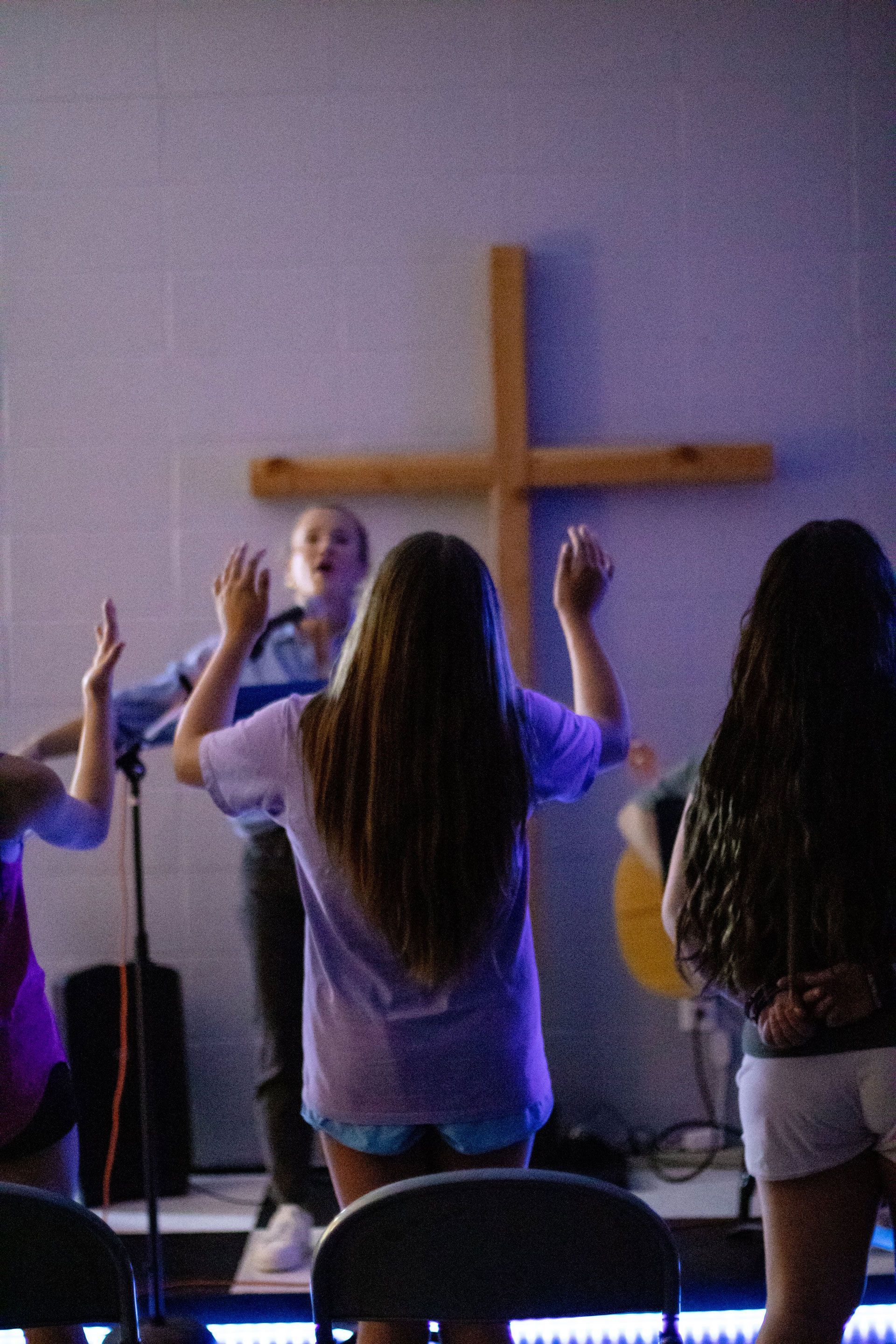 People standing with raised hands in front of a wooden cross during a church service