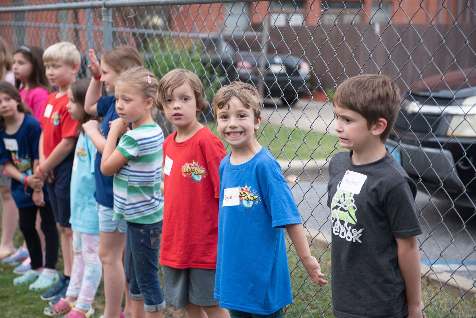 A group of children are standing in front of a chain link fence.