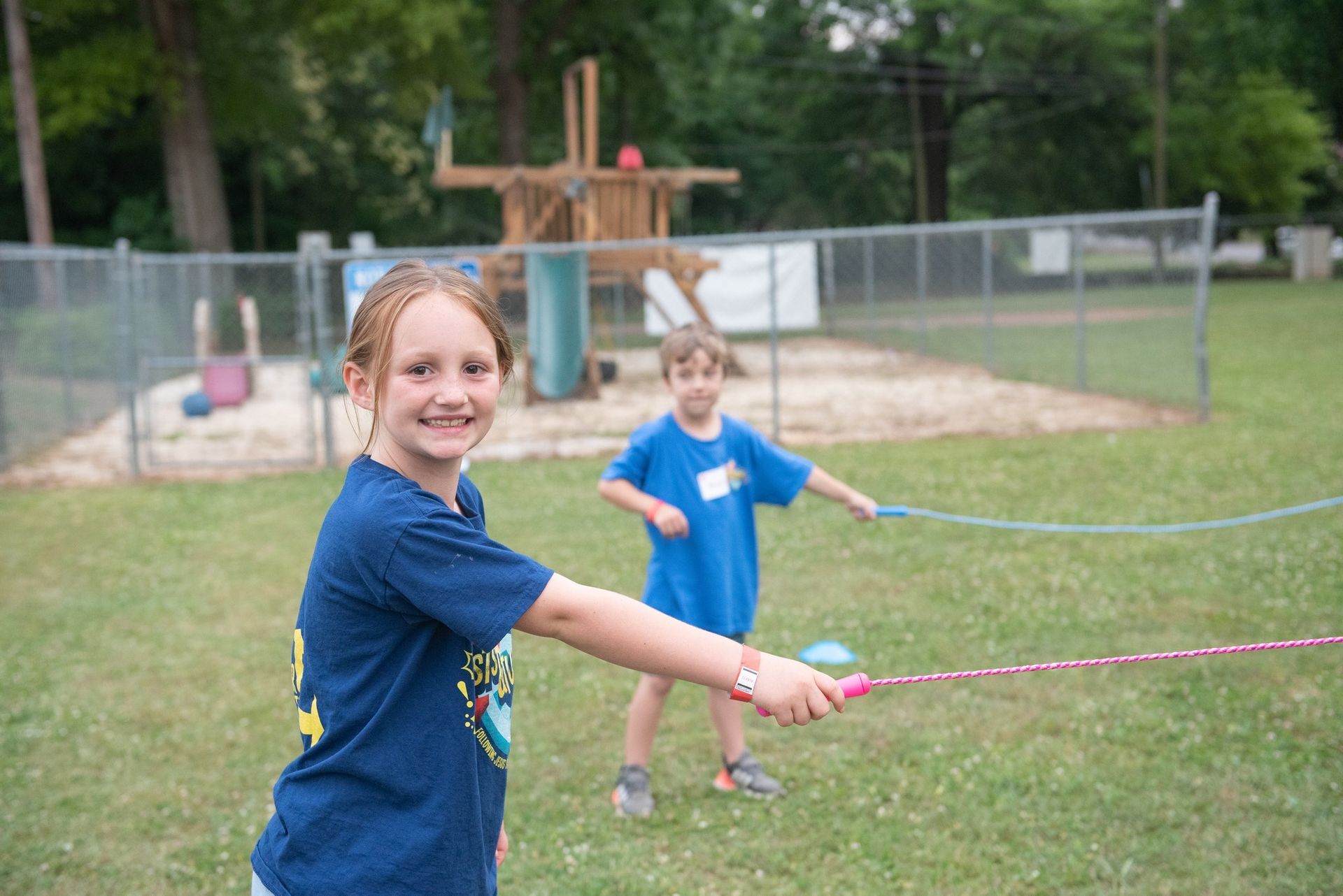 Two young girls are playing with a rope in a park.