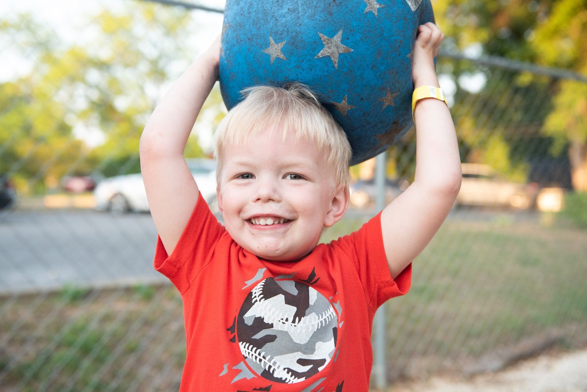 A young boy is holding a blue ball over his head.