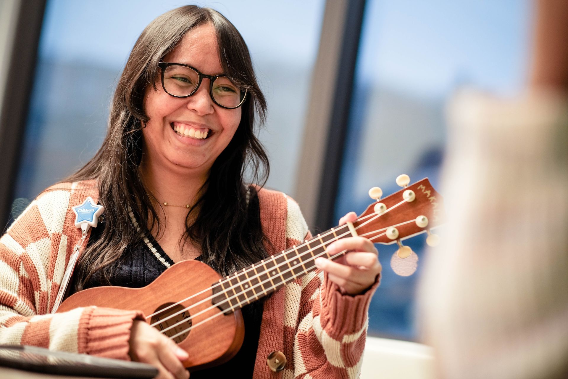Music therapist strums a ukulele while grinning at a patient