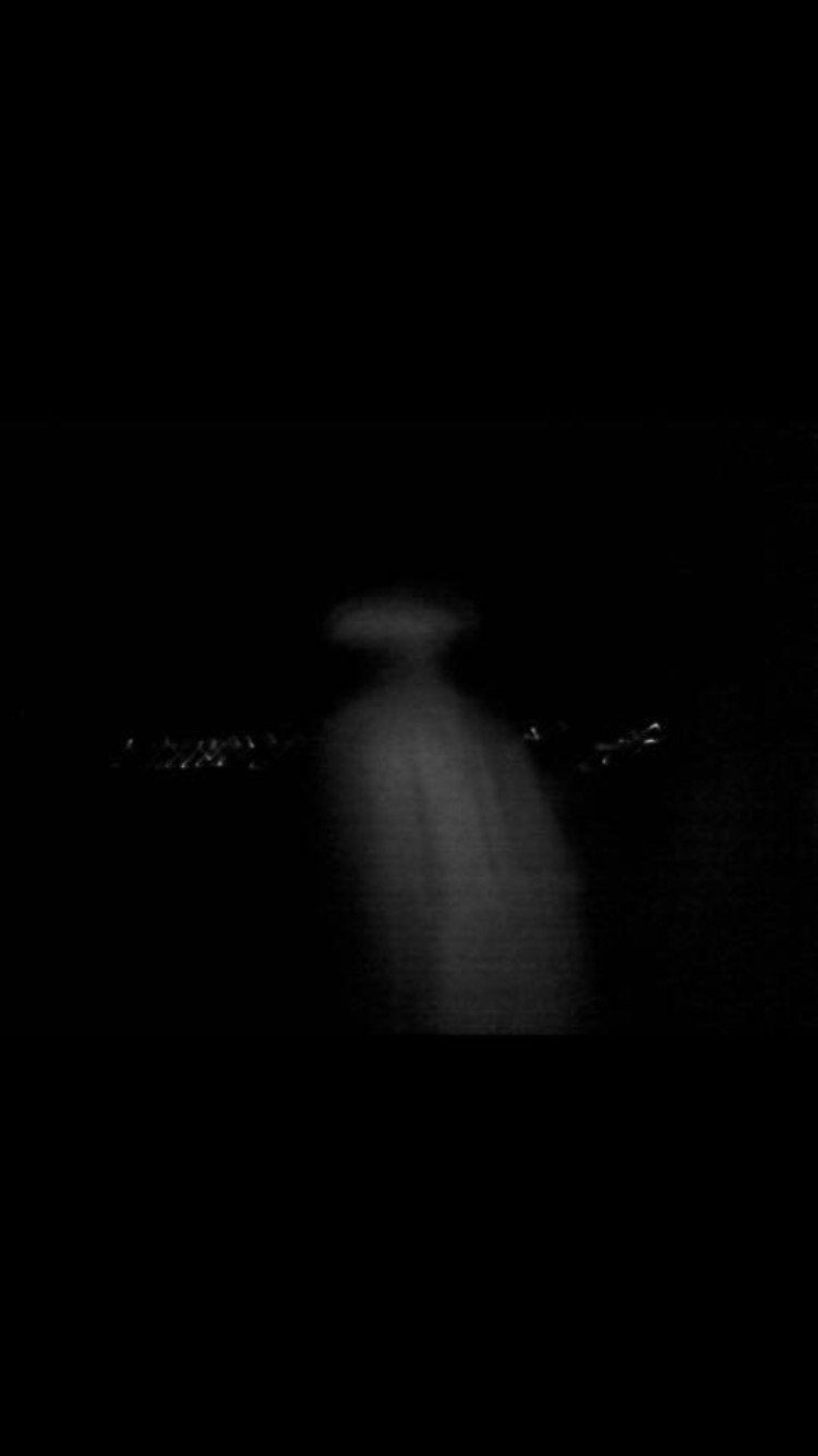 Blurry figure in a dark setting, faint cityscape lights in the distance.