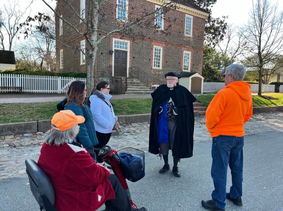 A costumed tour guide speaks to a small group in front of a brick building.