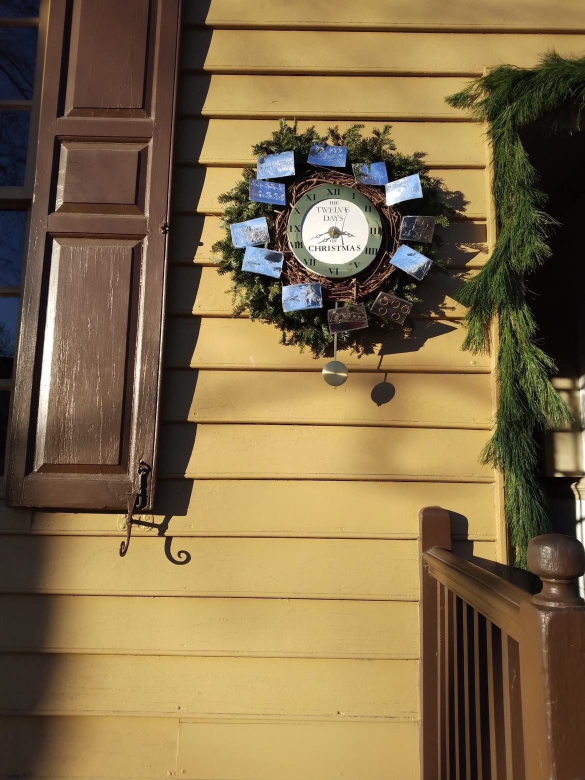 Yellow house with wreath. Brown shutters, garland, and railing.
