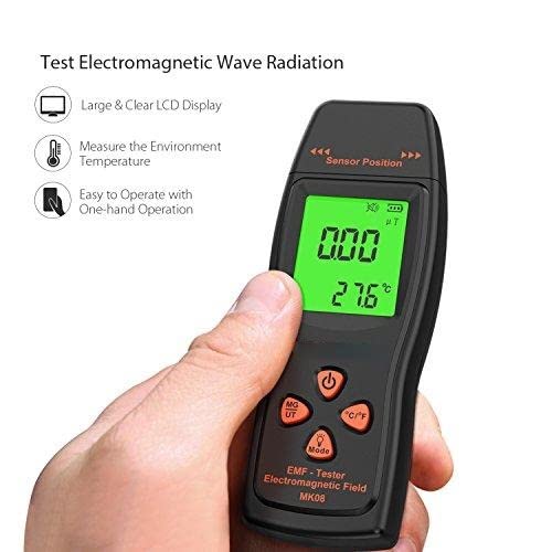 Hand holding a black electromagnetic wave radiation detector with a green display showing readings.